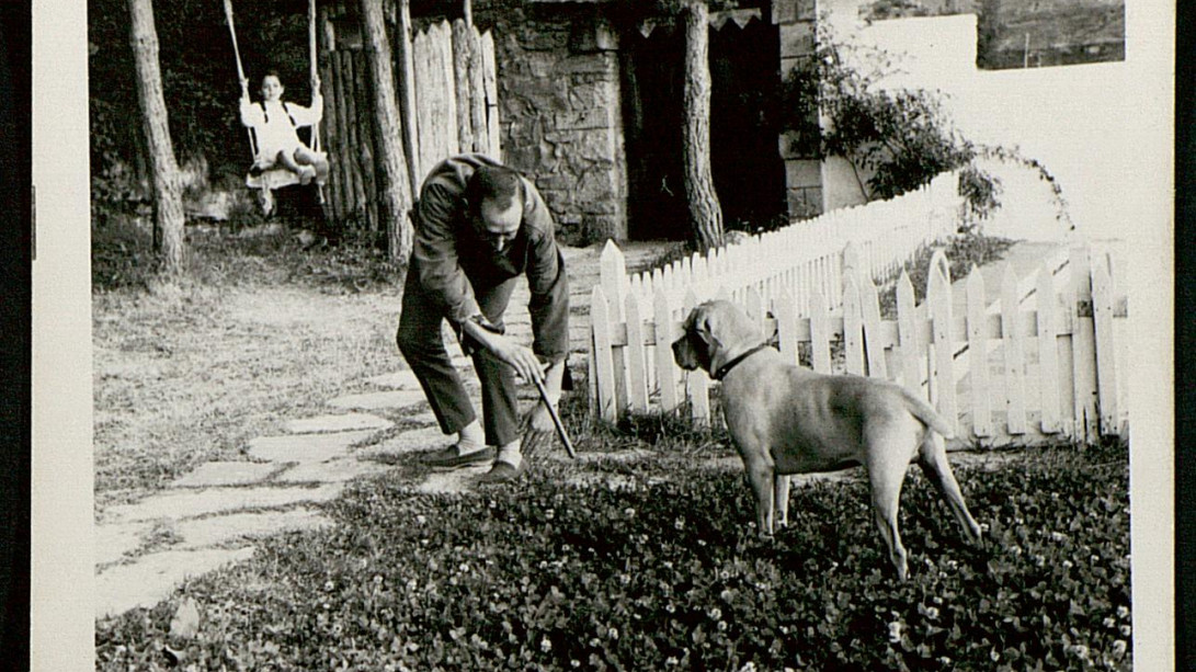 Fundación Miguel Delibes, AMD,122,78. Elisa Delibes de Castro observa a Miguel Delibes Setién jugando con un perro en su casa de Sedano (Burgos).